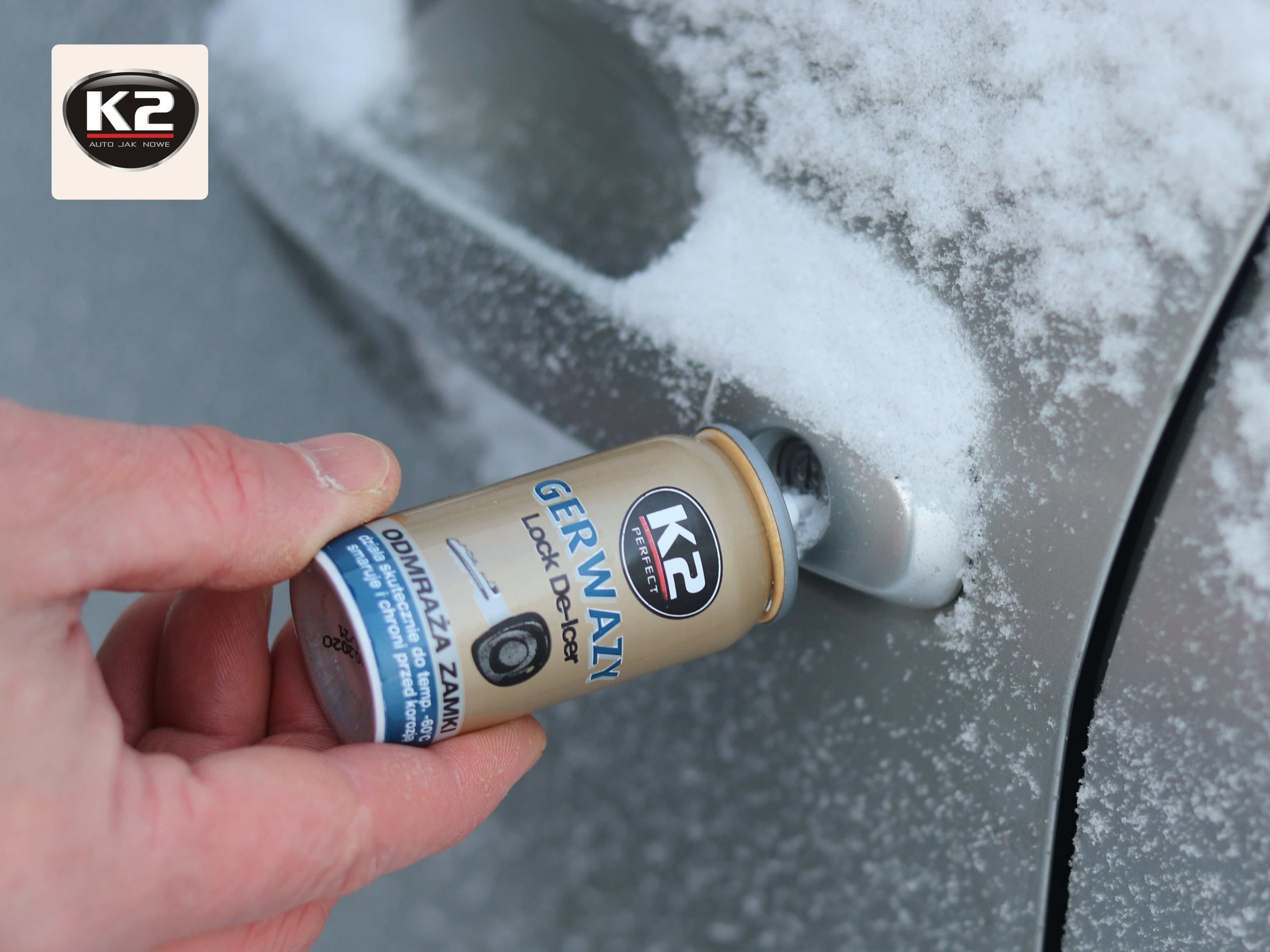 Ręka aplikuje odmrażacz do zamków K2 GERWAZY do zamarzniętej klamki samochodu.