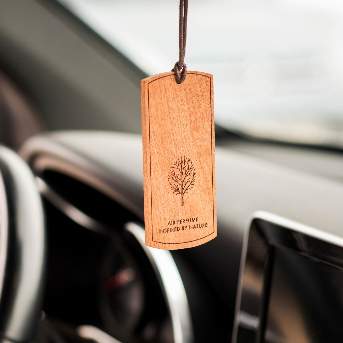 Elegancka drewniana zawieszka zapachowa K2 EVOS, z wygrawerowanym motywem drzewa i napisem Air Perfume Inspired By Nature, zawieszona we wnętrzu auta.