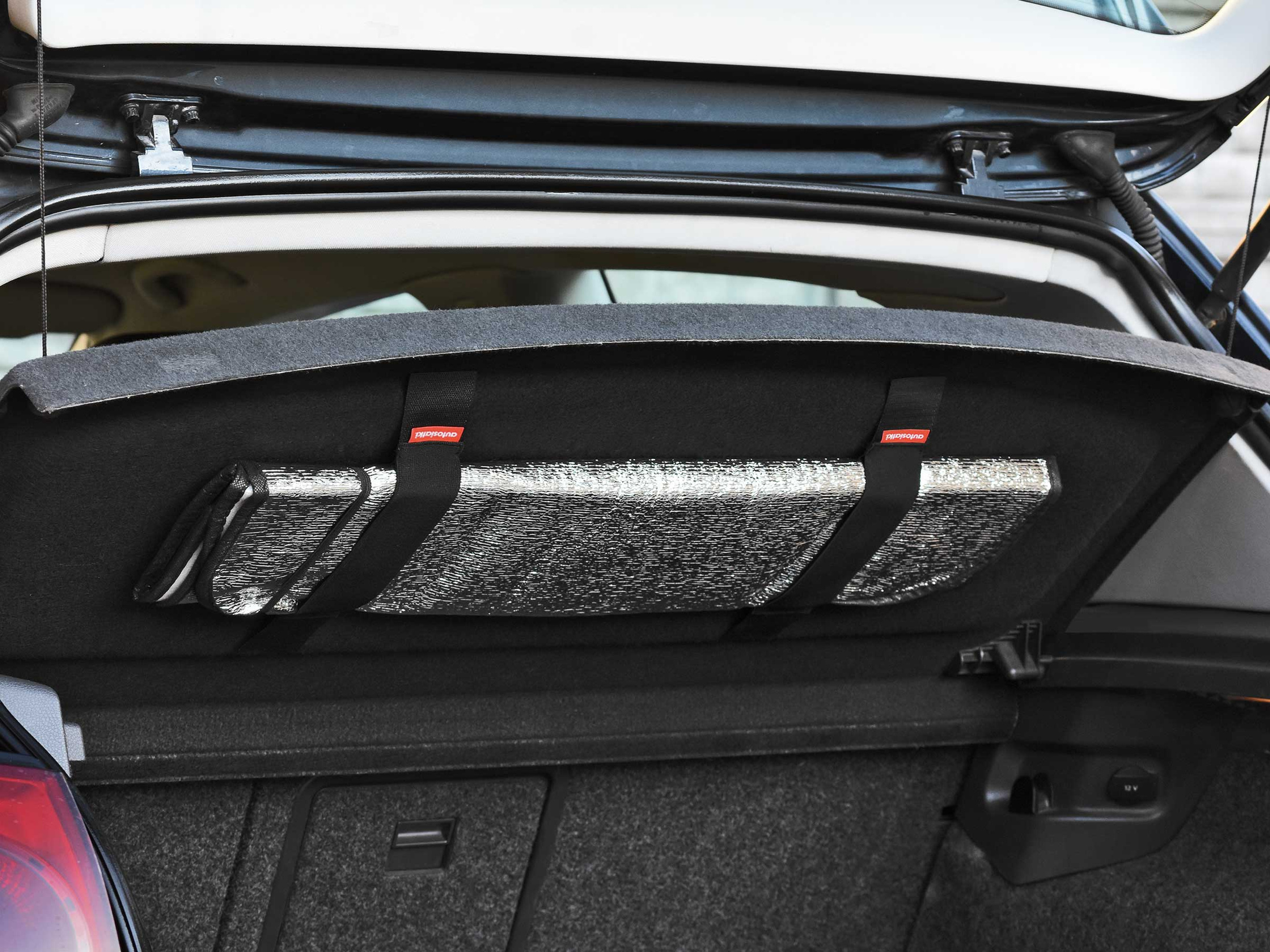 Szara mata antyszroniowa do przedniej szyby, zwinięta i stabilnie przymocowana w bagażniku za pomocą uchwytów na rzep.